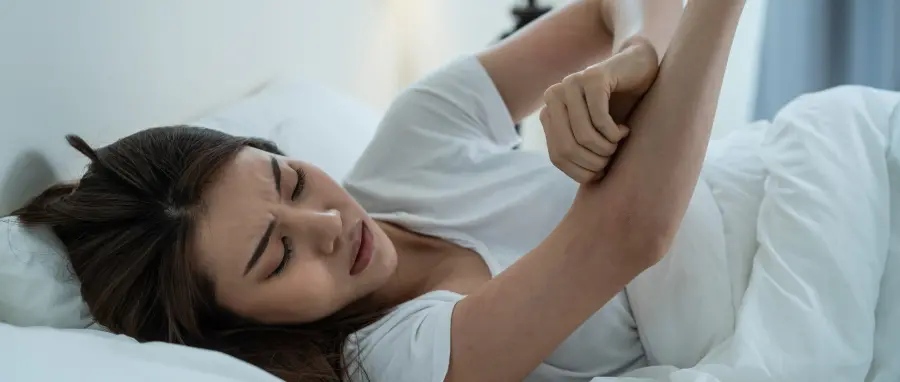 Young woman in bed scratching arm from bed bug bites