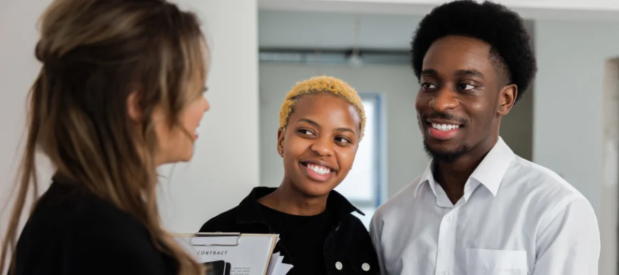Real estate agent handing house keys to a smiling young couple inside a modern apartment.